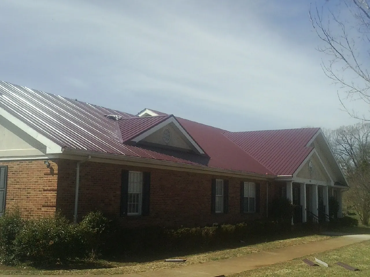 Red metal roof with gabled entries on a long brick building, from a Hail Damage Roof Repair job in Trevorton