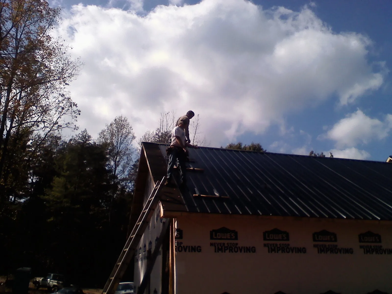 Roofer fastening dark metal panels high against a cloudy sky, from a Roof Inspection job in Trevorton