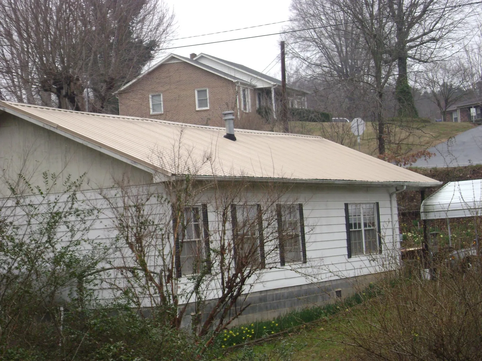 Tan metal roof on a white sided house set into a hillside — Commercial Roofing by Roofing Brothers in Trevorton